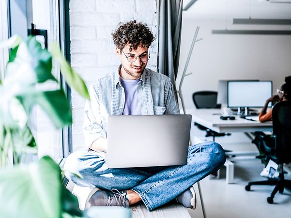 Junger lässig gekleideter Mann, der im Büro am Laptop arbeitet