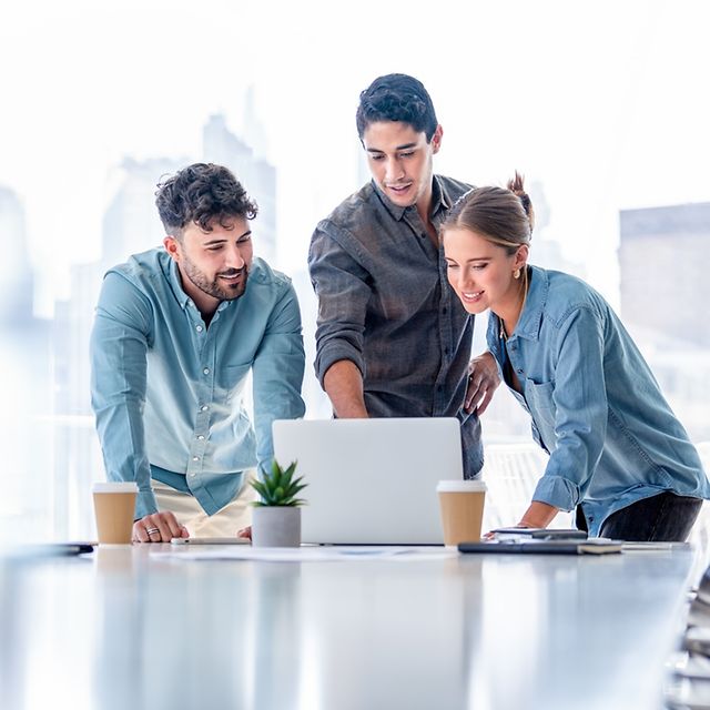 Three people are looking at a laptop screen and discussing a project.