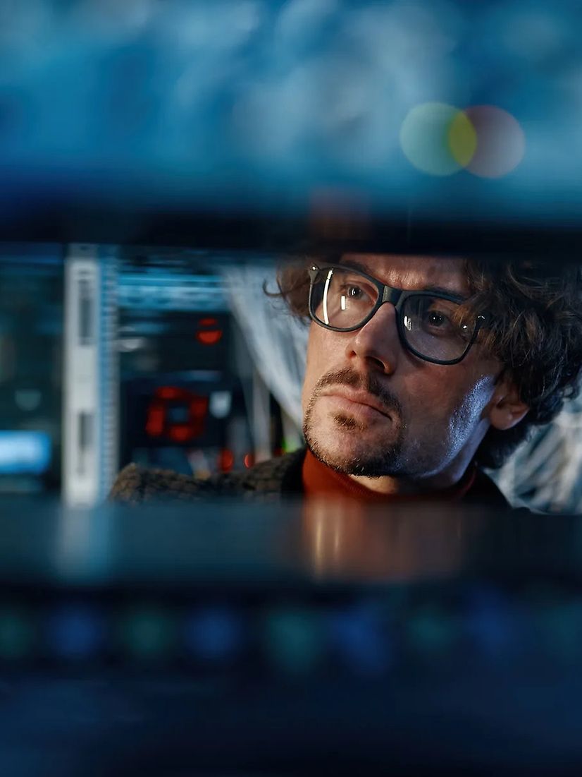Two people, a woman and a man, are talking to each other at a desk with lots of monitors.