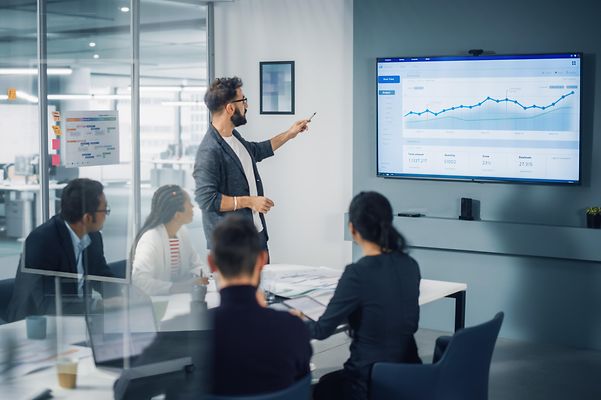View of a meeting room in which a male colleague is presenting visualised data