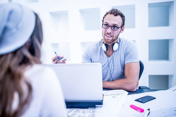 A man talks to a colleague with a friendly smile, looking over her shoulder.