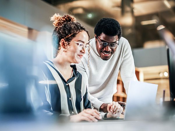 Portrait of two colleagues using a laptop to discuss Telekom's CRM consulting services