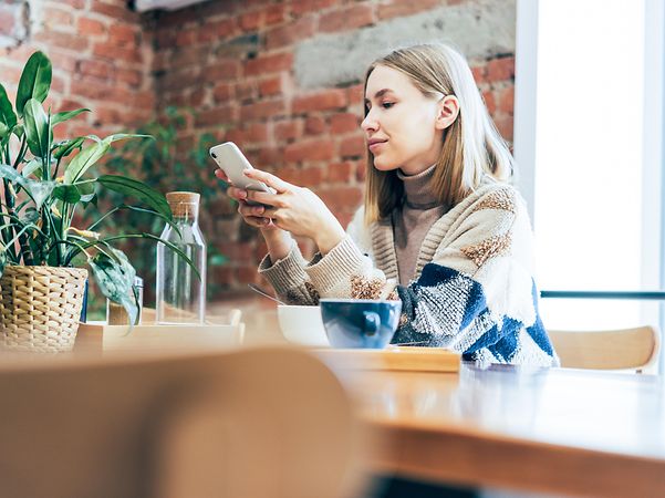 A businesswoman in a café checks her work on her mobile phone via Business VPN.