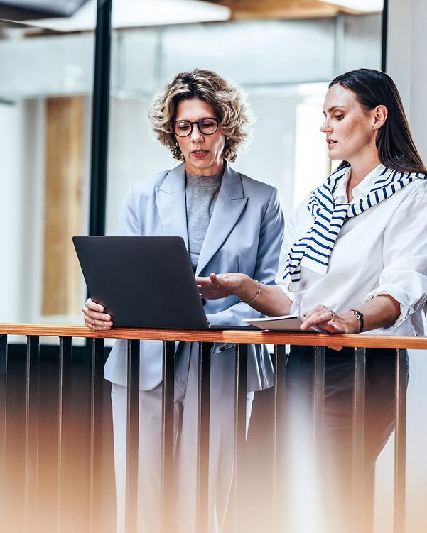 Two businesswomen discuss cloud infrastructure while using a laptop.