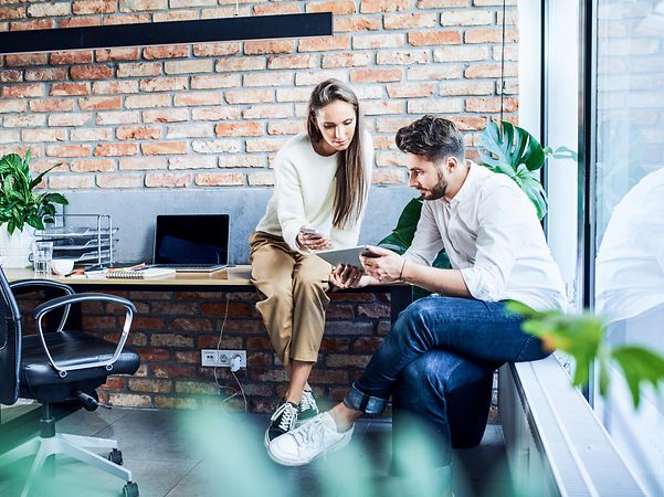 Businessman and businesswoman comparing ideas on a phone and tablet during a meeting in an office
