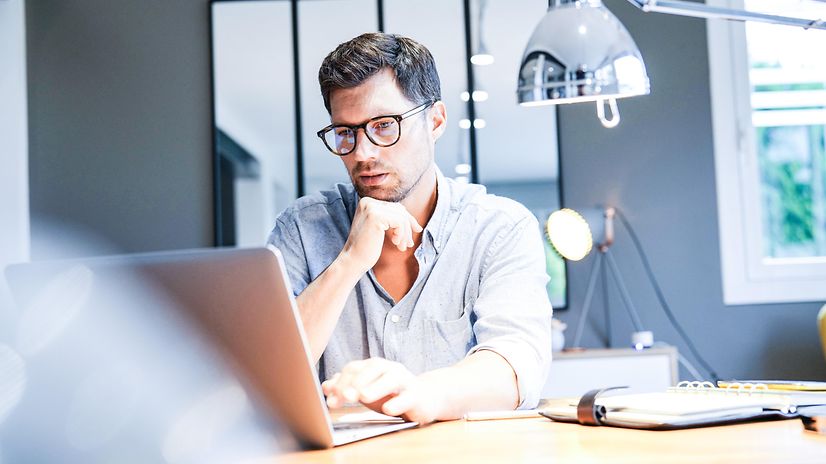 A man works on a laptop in a bright office and uses Interactive Voice Response Professional.
