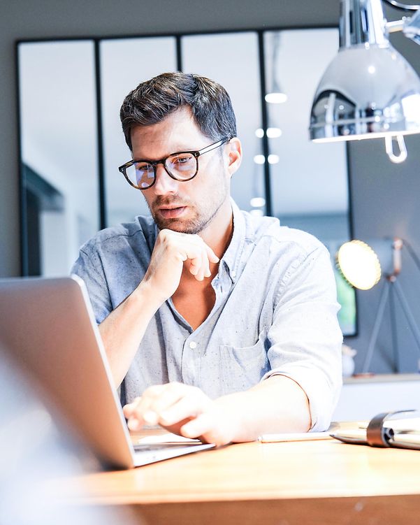A man works on a laptop in a bright office and uses Interactive Voice Response Professional.