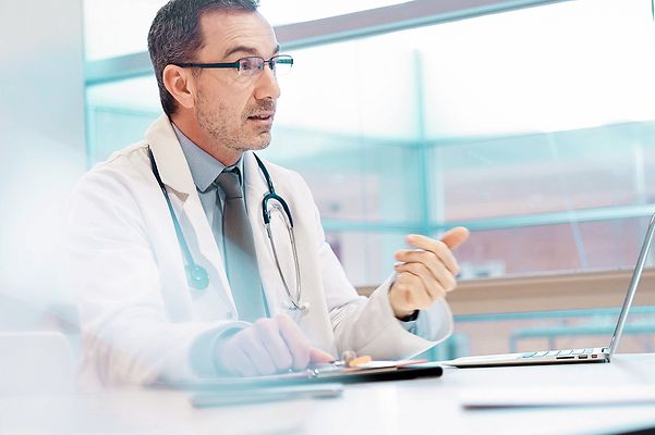 Doctor sitting in front of a laptop in his practice and using Telekom's telematics solution