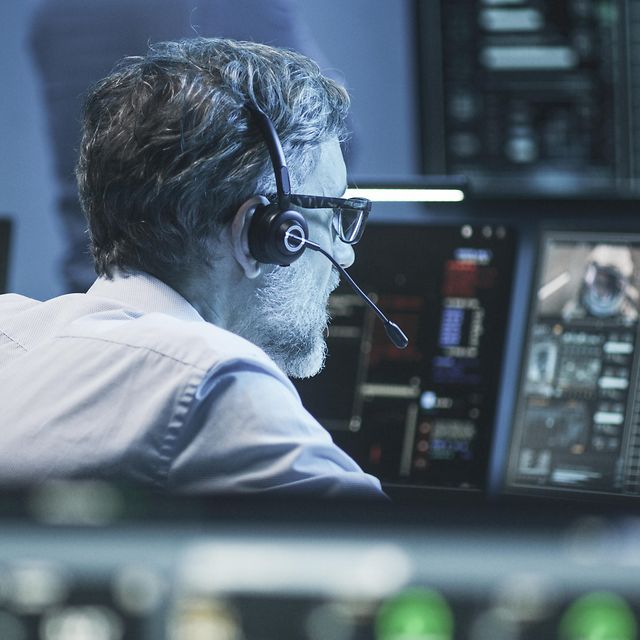 A man is wearing a headset and looking at a screen.
