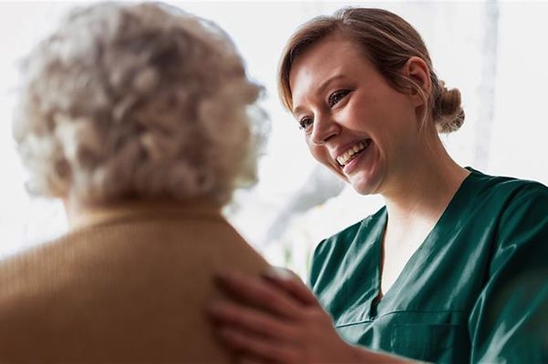 A nurse smiles as she places her hand on an elderly woman's back.