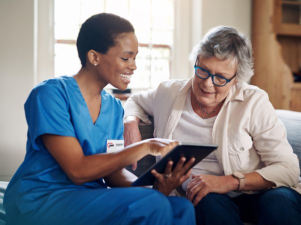 Smiling nurse from AWO Schwaben looks at an iPad with an elderly lady