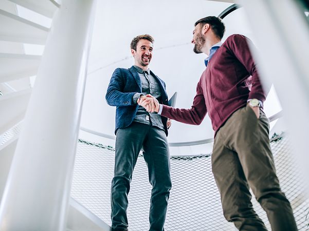 Two men in casual business attire shake hands.