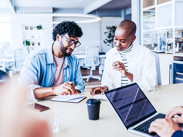 A team consisting of three people. Two are talking, while the third is working on a laptop.
