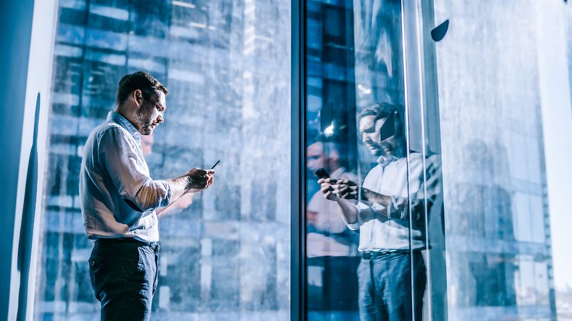 Man standing in front of a window, holding a smartphone protected by Samsung Knox