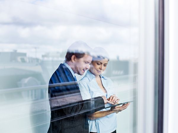Two adults in business attire look at the Telekom landline tariff advisor and product recommendations on a tablet.