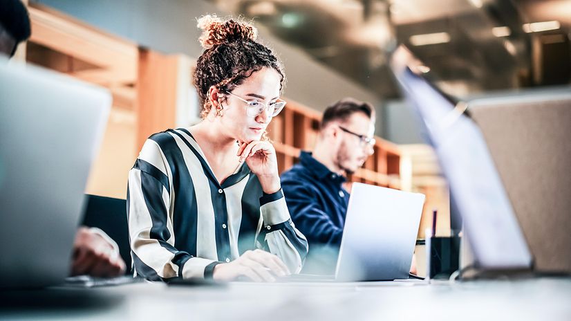 A woman is sitting and looking at her laptop.
