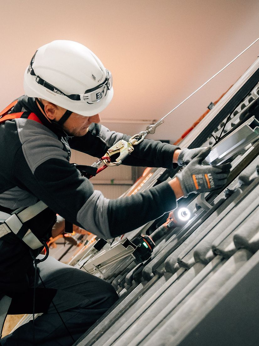 Enpal employee wearing a helmet and protective gear installs a solar power system on the roof.