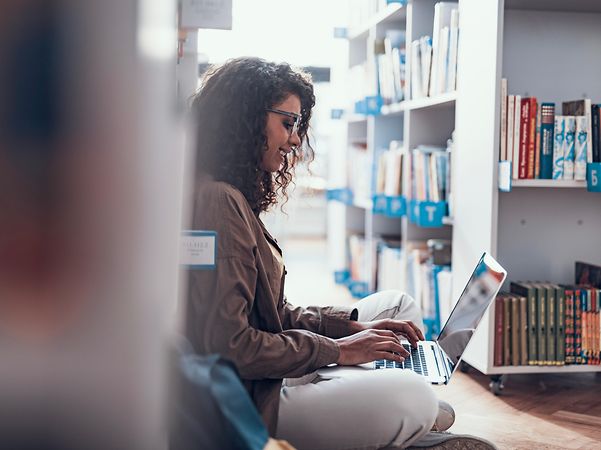 Frau sitzt in einer Bibliothek und informiert sich über Security OnNet Comfort