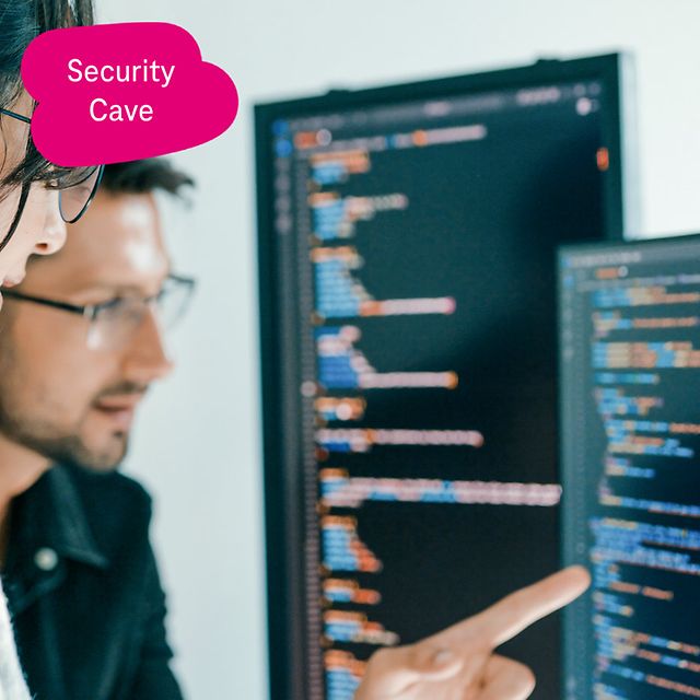 Zwei Personen analysieren Quellcode auf großen Monitoren, eine zeigt mit dem Finger auf den Bildschirm.
