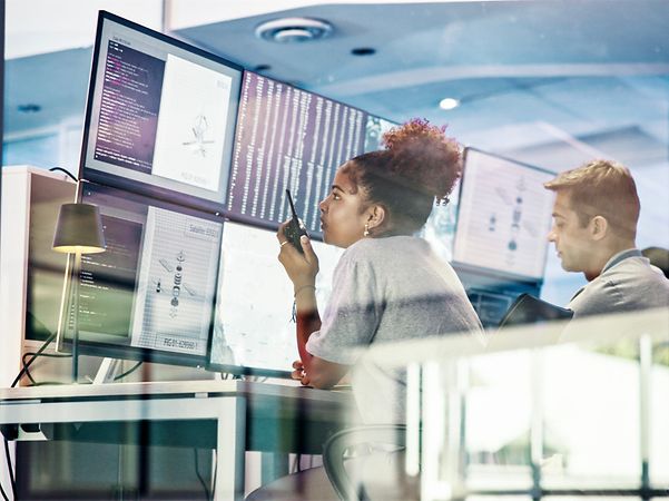 Zwei IT-Fachkräfte analysieren Daten auf mehreren Monitoren in einem Kontrollraum.