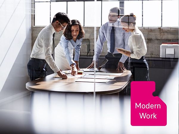 A working group in a modern office is gathered around a table discussing documents; photographed through a glass wall
