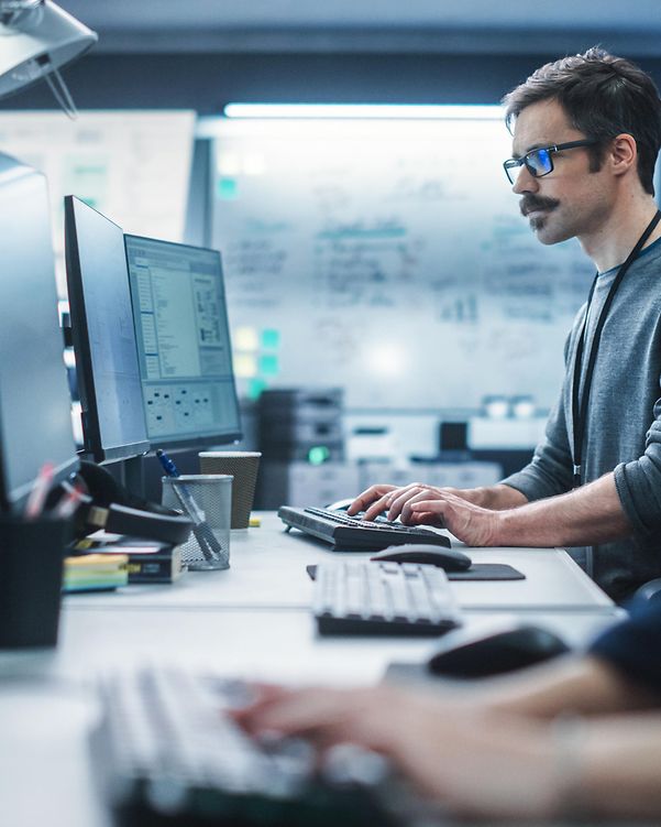 Porträt eines nachdenklichen Ingenieurs, der an einem Desktop-Computer in einer technologischen Büroumgebung arbeitet.