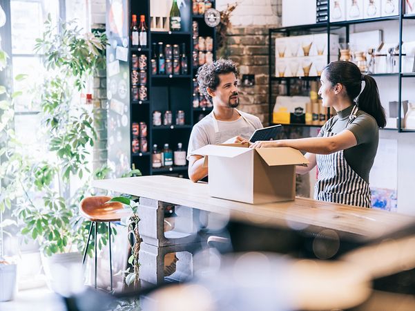 Zwei Mitarbeitende füllen ein Paket, nachdem sie ihre Produkte erfolgreich über ihren Webshop online verkauft haben.