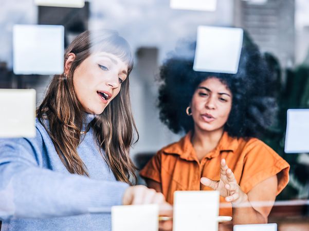 Zwei Frauen diskutieren mit Hilfe von Post-its geeignete Domain Namen für den Internetauftritt ihres Unternehmens.