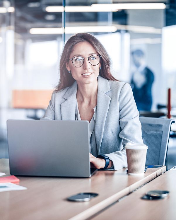 Lächelnde Geschäftsfrau mit Brille, die in einem modernen Büro in einem Unternehmen an einem Laptop arbeitet