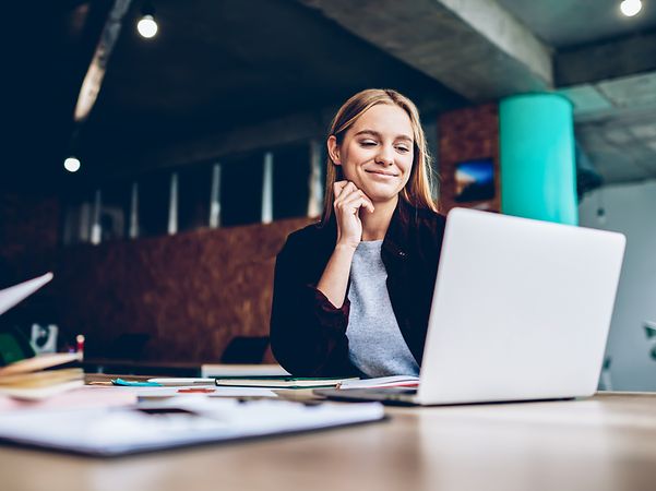 Junge Frau hat erfolgreich DocuSign verwendet und sitzt lächelnd vor dem Laptop.