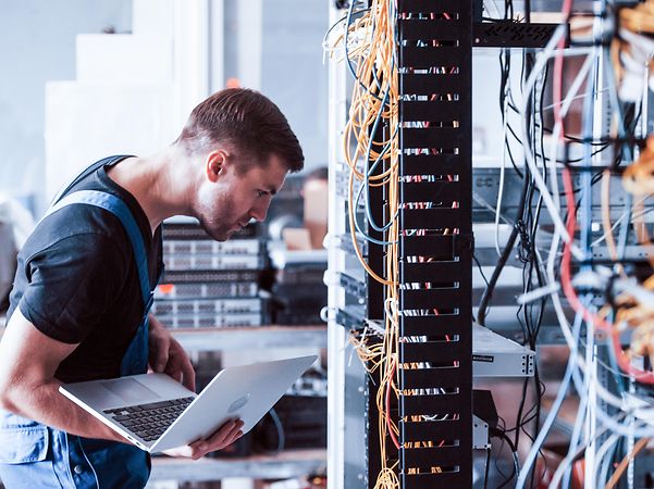 Ein Techniker mit Laptop vor einem Serverschrank für Magenta Secure SD-WAN auf Basis Fortinet