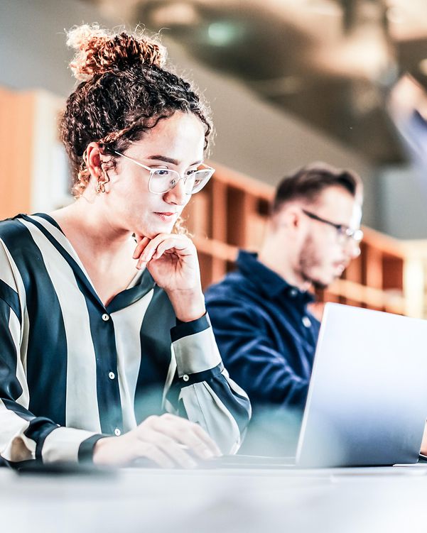 Porträt einer hispanischen jungen Frau, die in einem modernen hellen Büro am Computer arbeitet. 