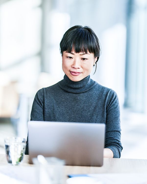 Lächelnde japanische Geschäftsfrau, die im Büro am Laptop arbeitet.