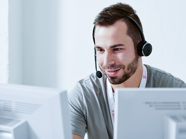 Ein Mann sitzt lächelnd mit Headset vor zwei Monitoren