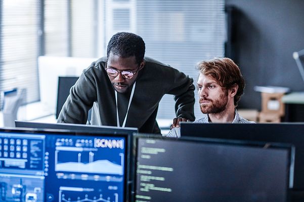 Zwei männliche Kollegen arbeiten im vier-Augen-Prinzip vor zwei Monitoren