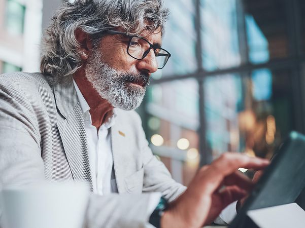 Mann sitzt in einem Café und nutzt ein Tablet.