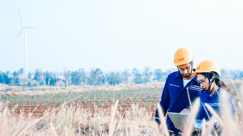 Zwei Techniker auf einem Feld nutzen Salesforce Energy & Utilities Cloud am Laptop, im Hintergrund Windräder