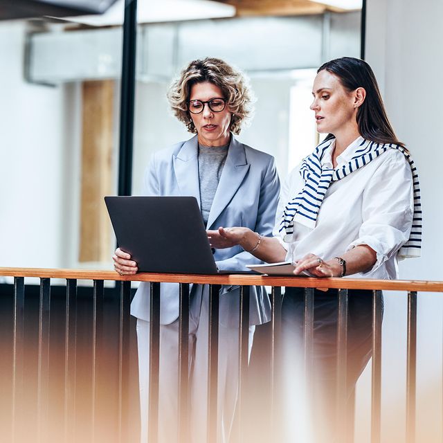 Zwei Geschäftsfrauen diskutieren miteinander, während sie einen Laptop benutzen 