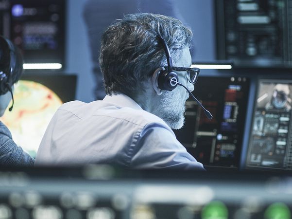 Mann sitzt mit Headset vor Computerbildschirmen
