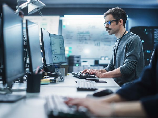 Porträt eines nachdenklichen Ingenieurs, der an einem Desktop-Computer in einer technologischen Büroumgebung arbeitet.