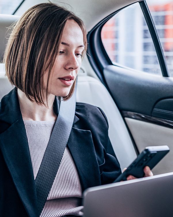 Eine Geschäftsfrau sitzt im Auto und hält eine Microsoft Teams Konferenz