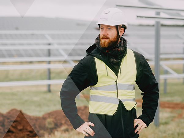 MaxSolar Mitarbeiter in gelber Schutzkleidung mit weissem Helm auf einem Solarfeld