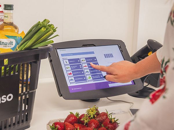 Grauer Einkaufskorb von tanteenso mit Waren neben Kasse zum Selbstcheckout