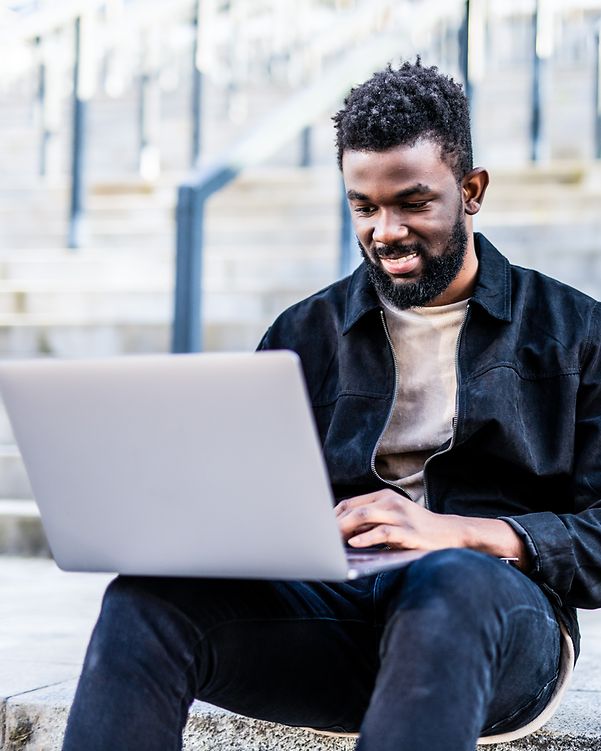 Ein junger Mann tippt auf seinem Laptop und lächelt