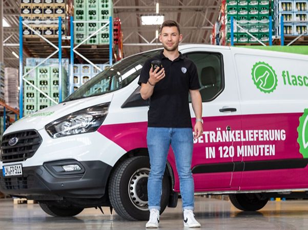 Mitarbeiter mit Handy vor seinem Lieferfahrzeug von flaschenpost