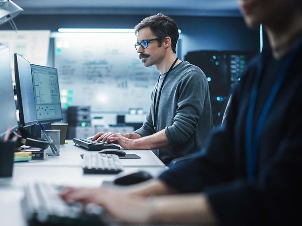 Porträt eines nachdenklichen Ingenieurs, der an einem Desktop-Computer in einer technologischen Büroumgebung arbeitet.