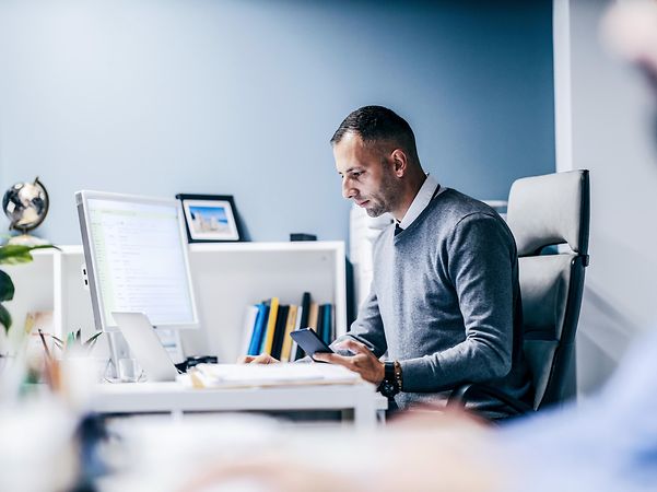 Ein Geschäftsmann sitzt im Büro und arbeit mit Laptop und Smartphone. 