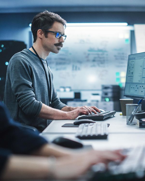 Ein Security Spezialist arbeitet an einem Desktop-Computer und überwacht IT-Systeme mittels Cyber Defense Lösungen