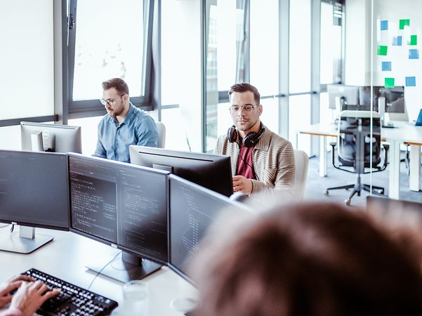 Mehrere Kollegen sitzen im Büro und lauschen einem Zoom X Webinar