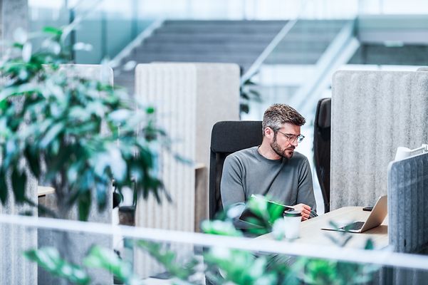 Ein Kollege sitzt im Büro und schaut auf sein Notebook mit Zoom X Rooms